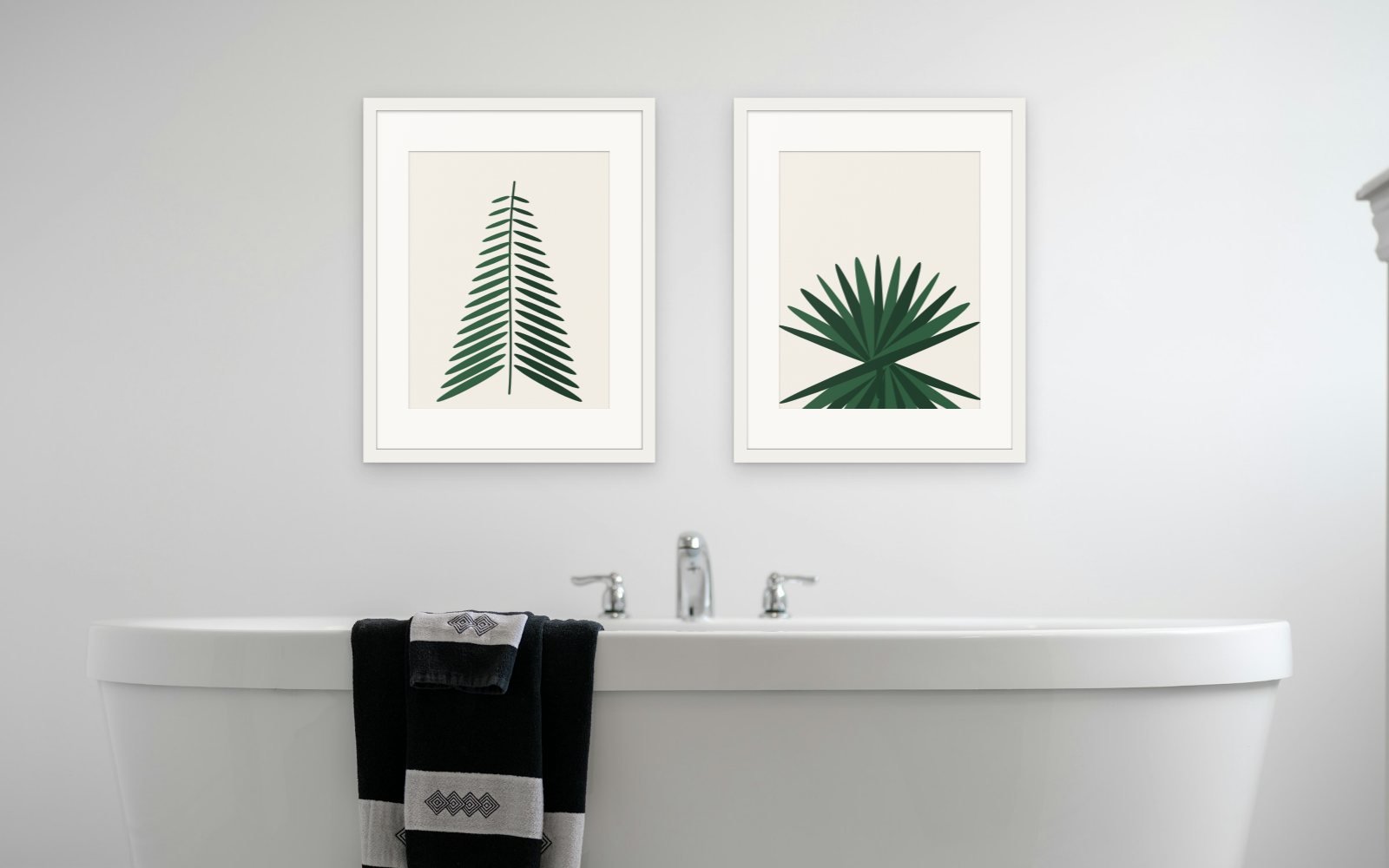 Two Paper Cuts prints in white frames above a freestanding bathtub in a bright white bathroom.